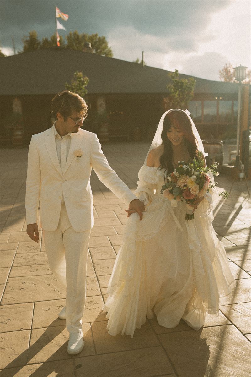 Groom leading the bride across a sunlit courtyard, her vintage gown and bouquet catching the late afternoon light