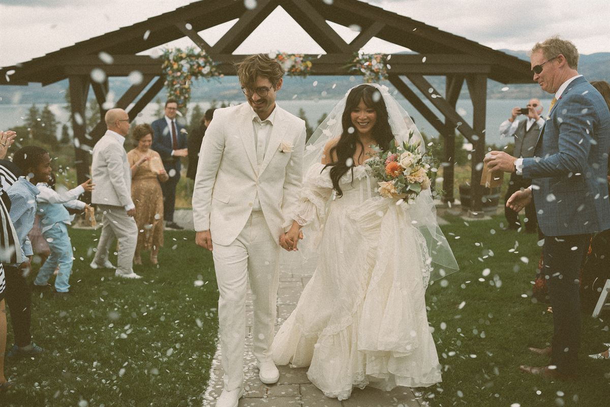 Guests throwing confetti over the newlyweds as they leave a timber pavilion