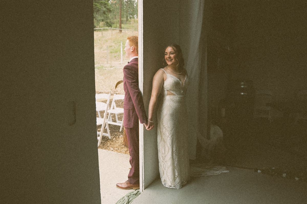 First touch before the ceremony, the groom in a burgundy suit reaching back around a doorway