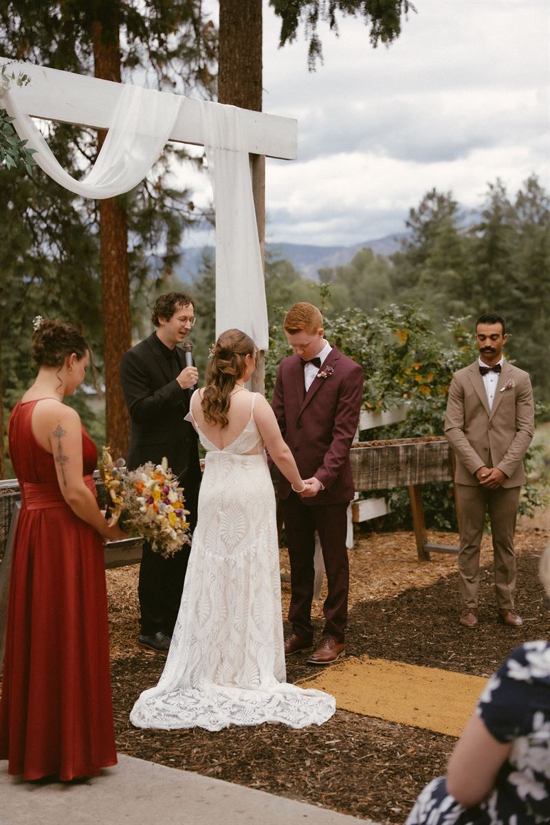 Couple exchanging vows beneath a draped wooden arbour at an Okanagan ceremony