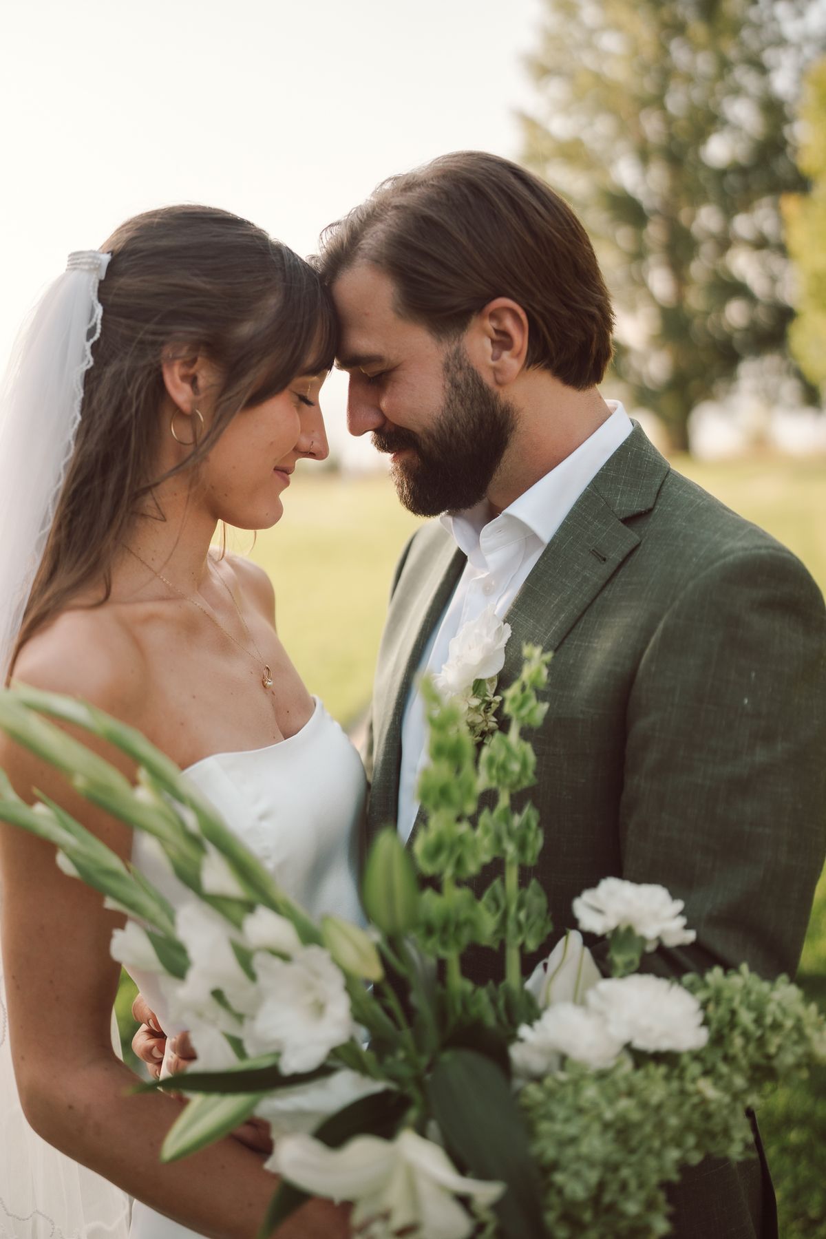 The couple touching foreheads as the bride holds her white lilies