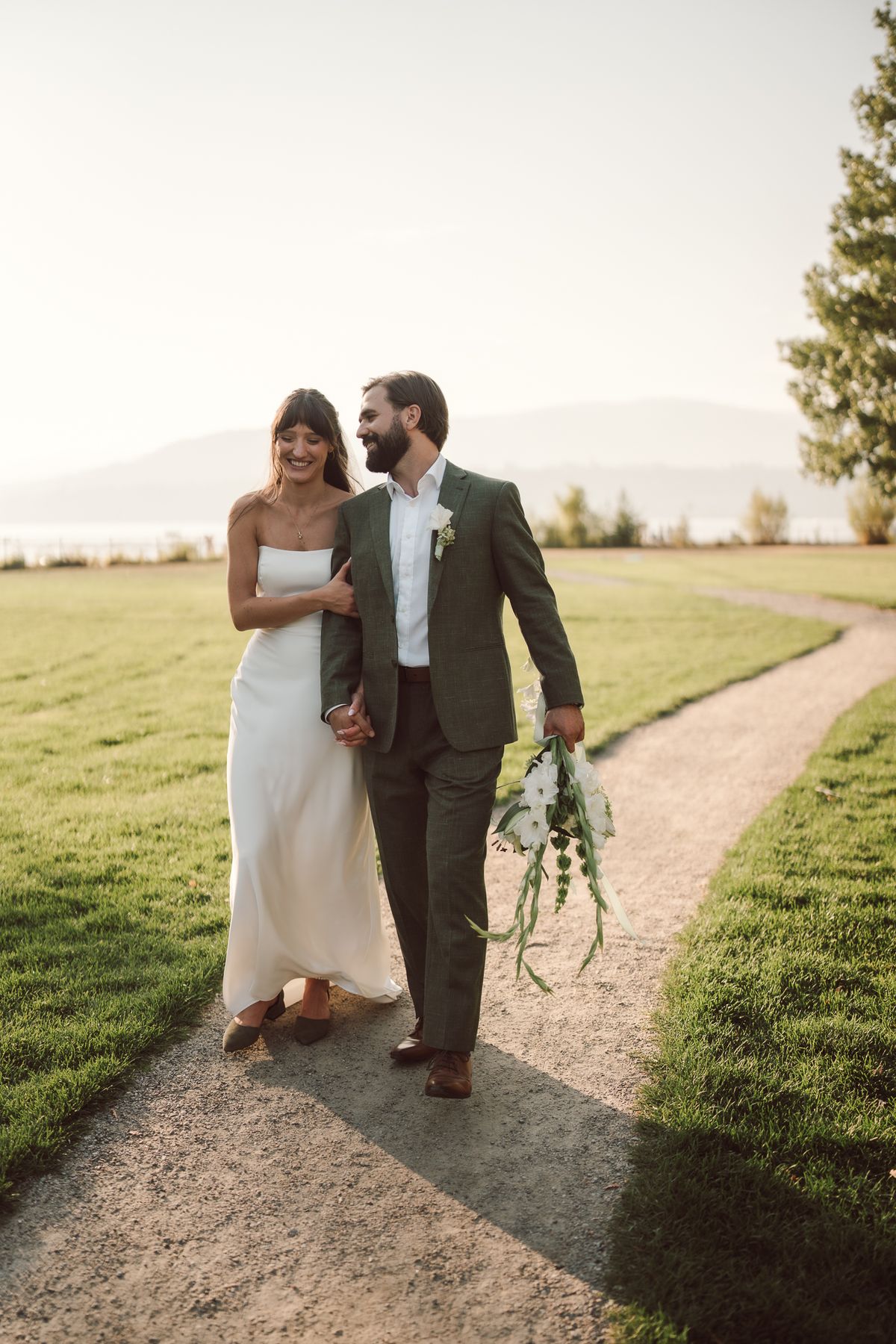 Mariah and Ryan walking a path with the lake and hills behind at golden hour