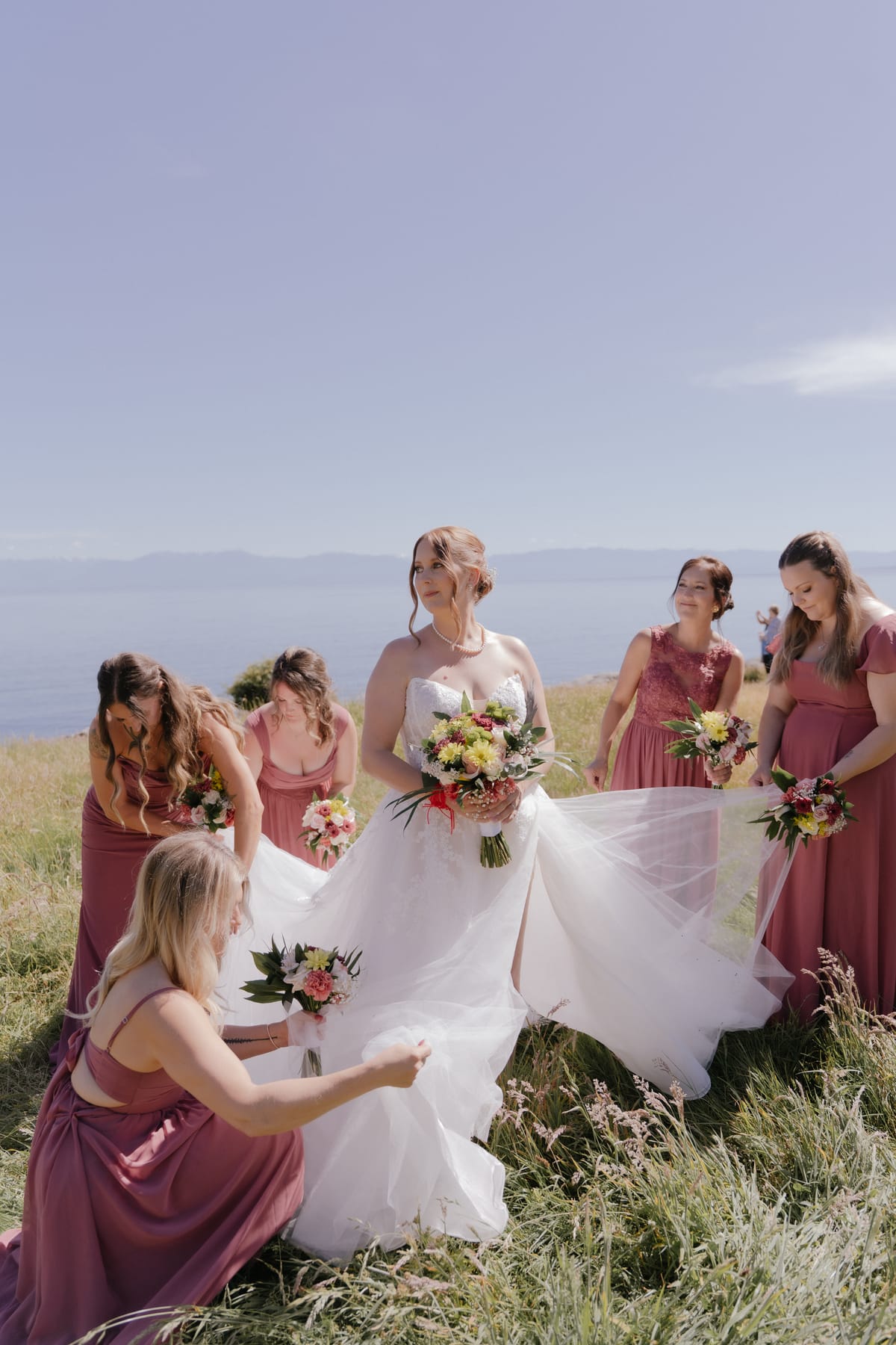 Bridesmaids fixing Charlotte's train on the bluff above the ocean