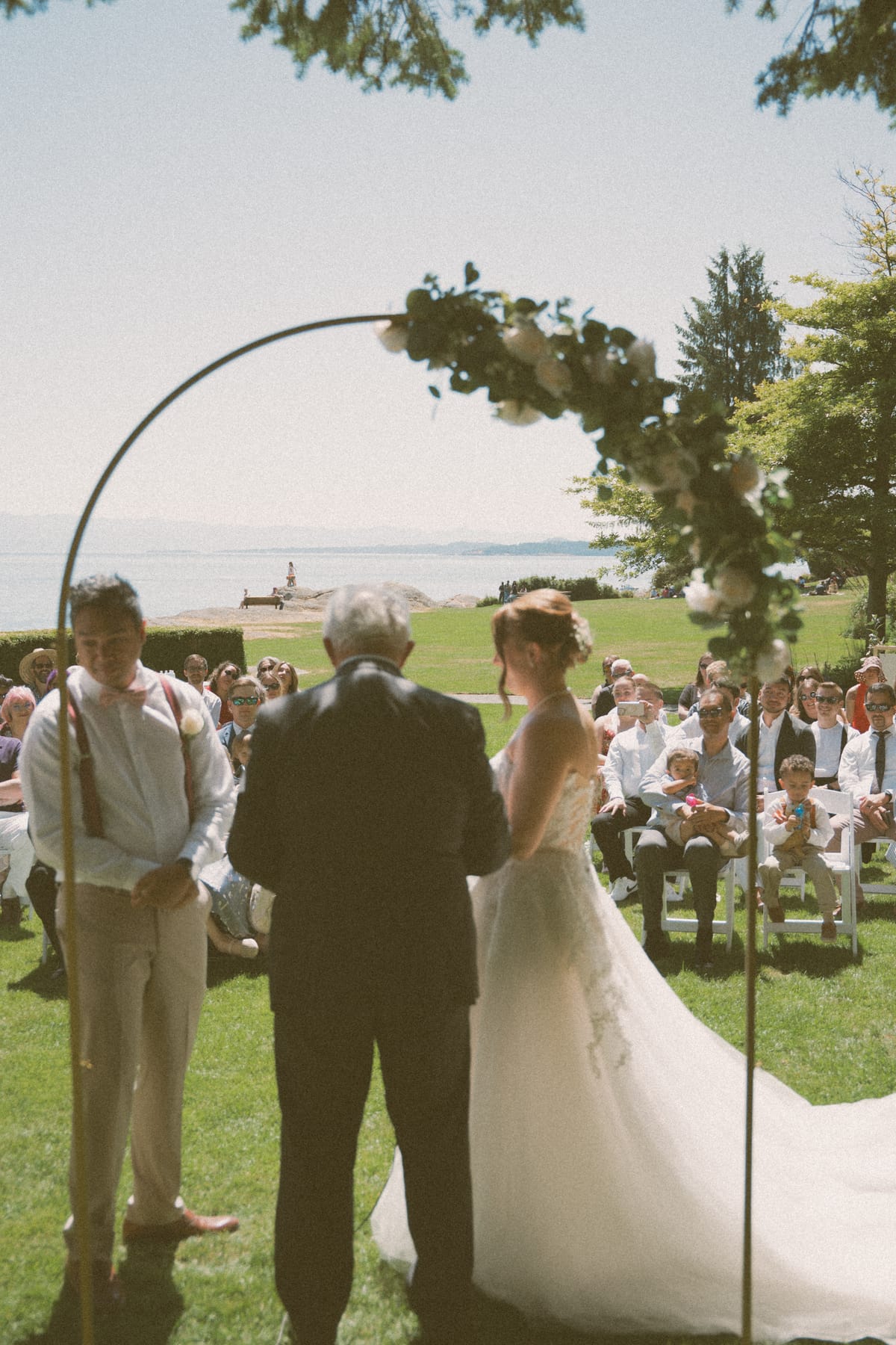 Charlotte and Vis exchanging vows at the arch with the strait and lighthouse beyond
