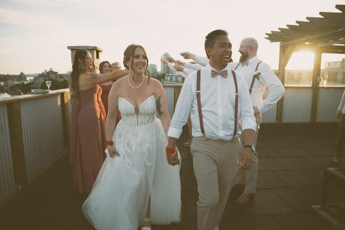 Charlotte and Vis entering their golden-hour rooftop reception to cheers