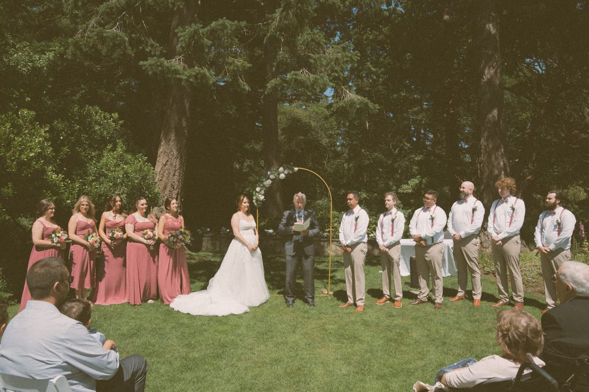 The seaside ceremony beneath the arch with the wedding party on the lawn
