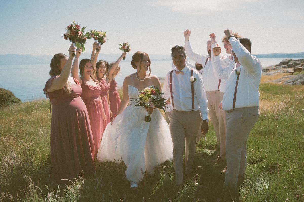 The wedding party cheering with the couple on the grassy oceanfront bluff