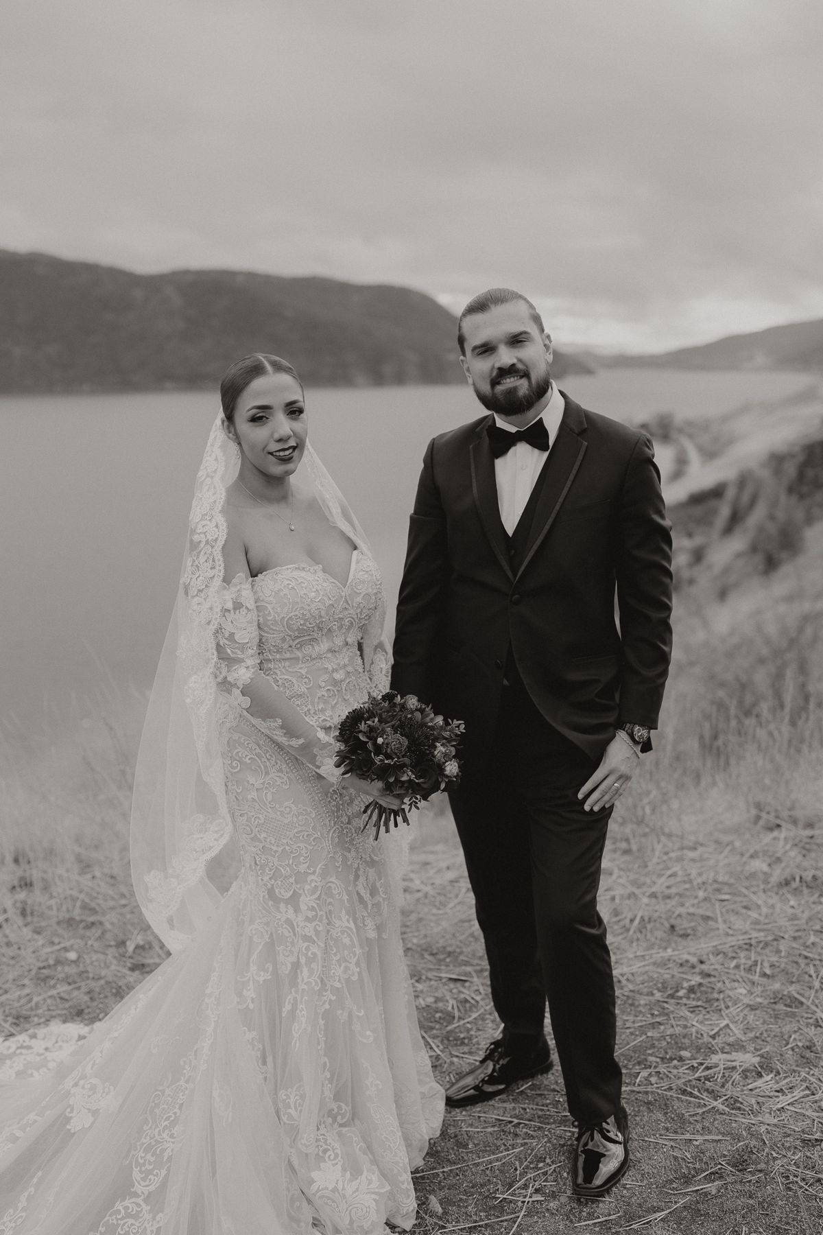 Carolyn and Rigaud on the hillside above the lake, the bride holding a deep-red bouquet