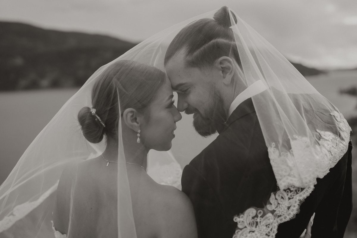 Black and white of the couple beneath the veil, foreheads together