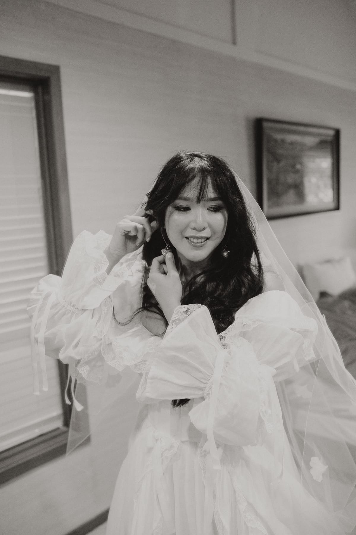 Black and white of Nina smiling as she fixes her veil and earring