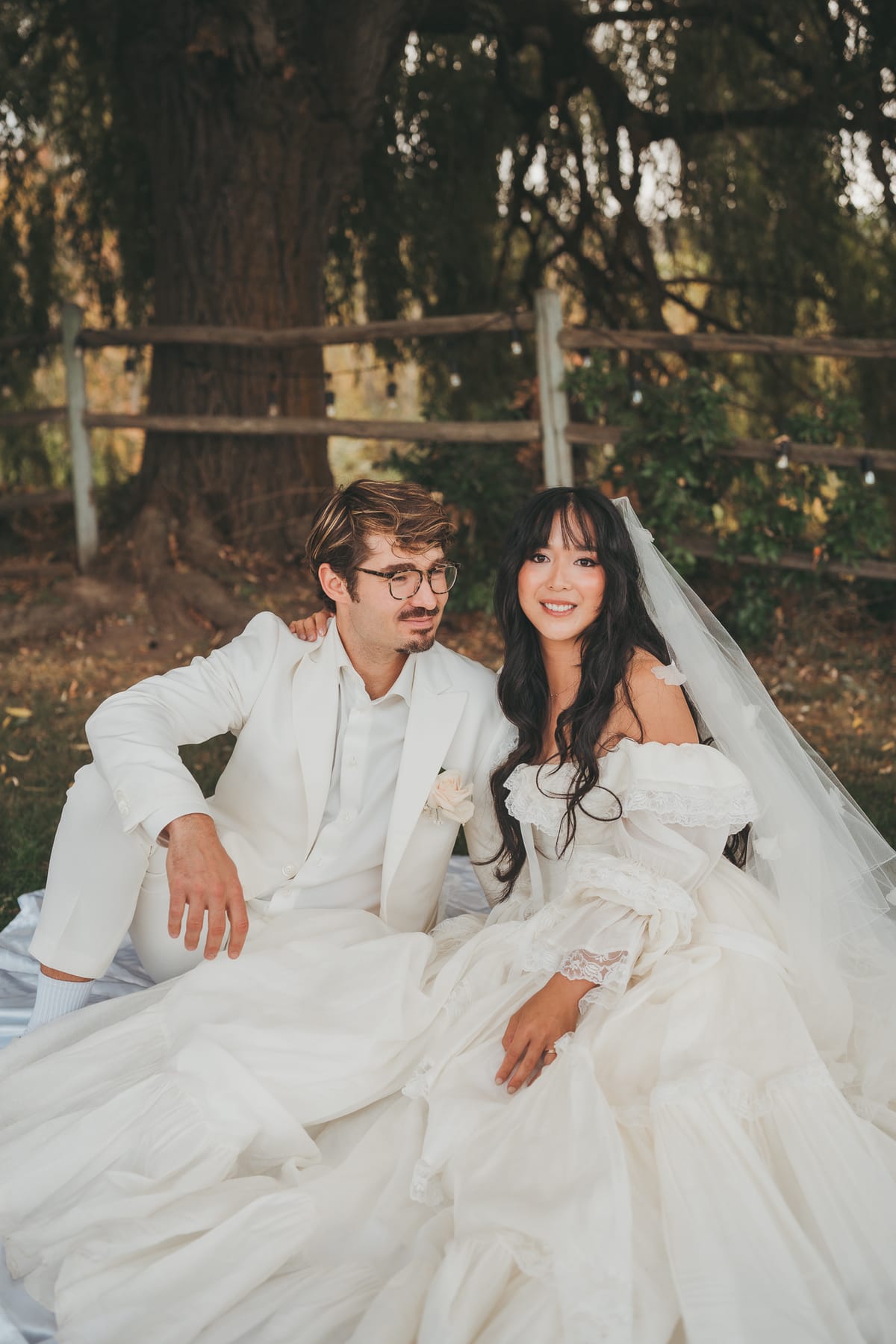 Nina and Brandon smiling together on the blanket beneath the willow