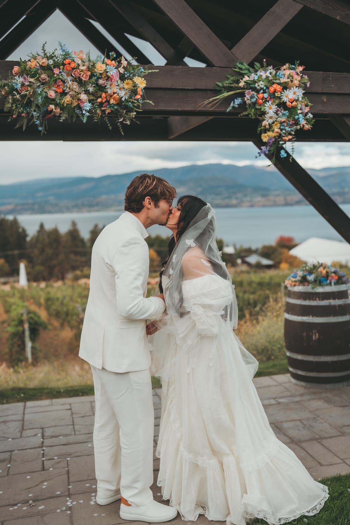 Nina and Brandon's first kiss under the flower-topped pergola with Okanagan Lake behind