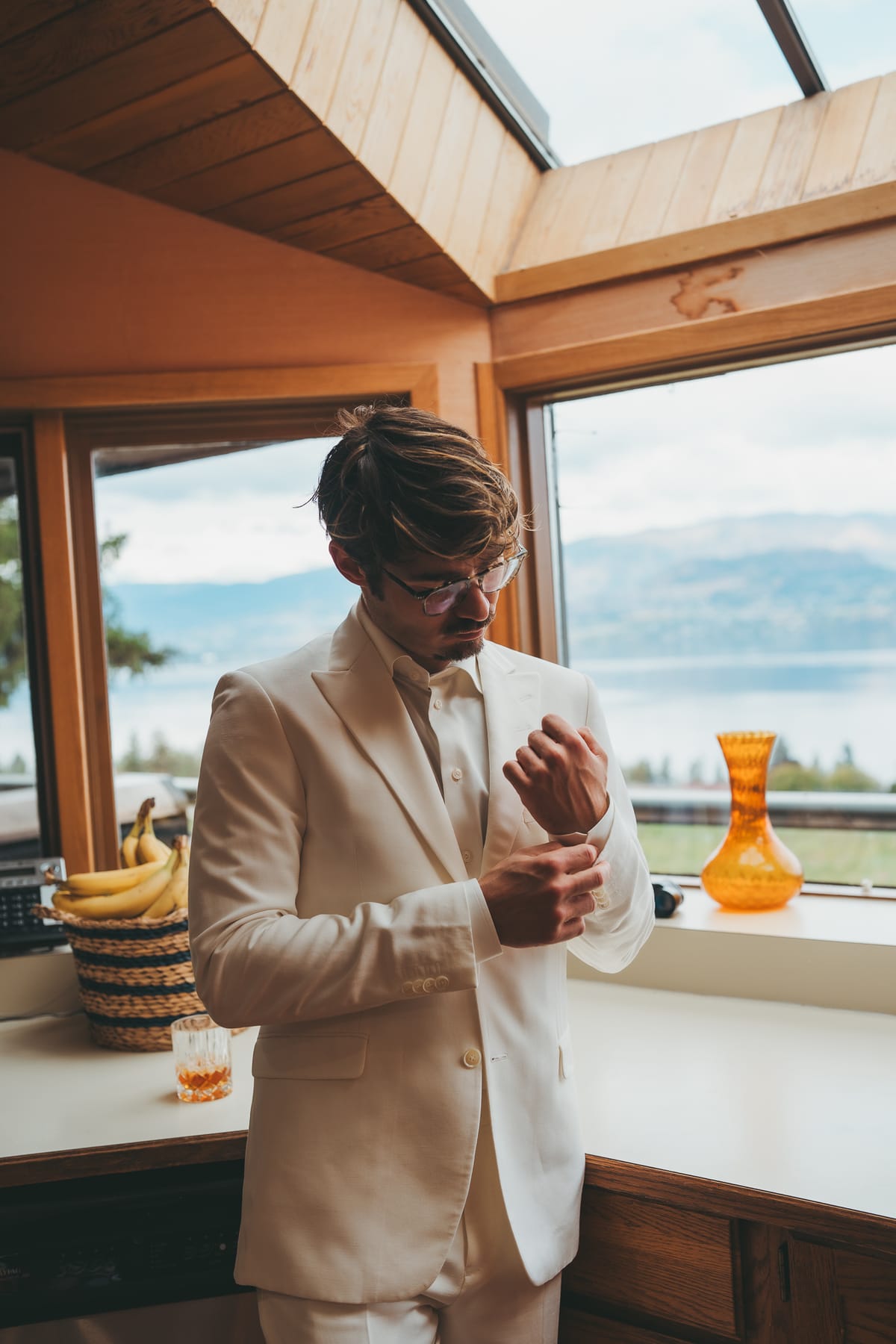 Brandon buttoning his cuff in the window light as he gets ready above the lake