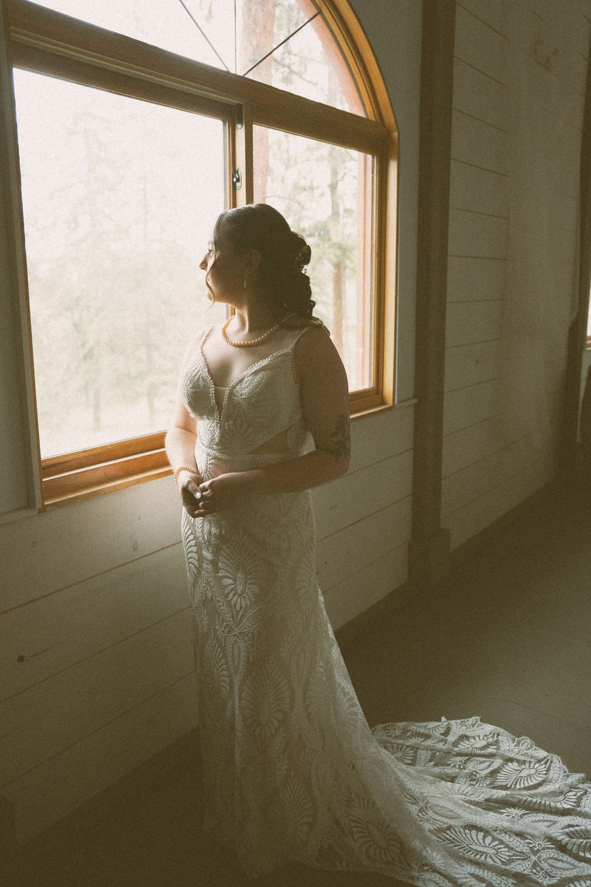 Bride in her lace gown backlit by a window as she gets ready