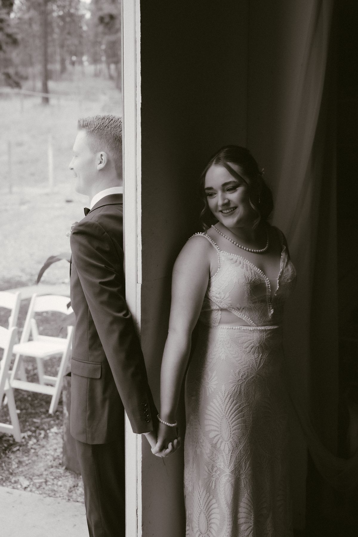 Black and white first touch, bride and groom holding hands around a corner