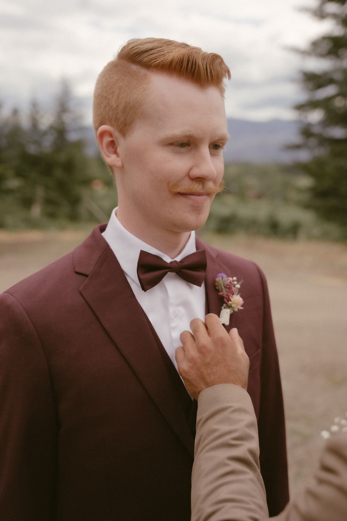 Portrait of the groom in his burgundy suit adjusting his cuff