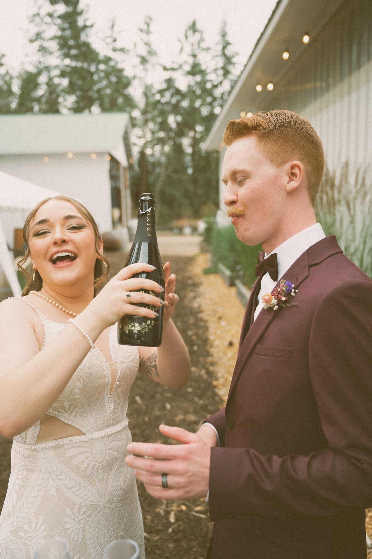 Bride and groom laughing over a bottle of champagne