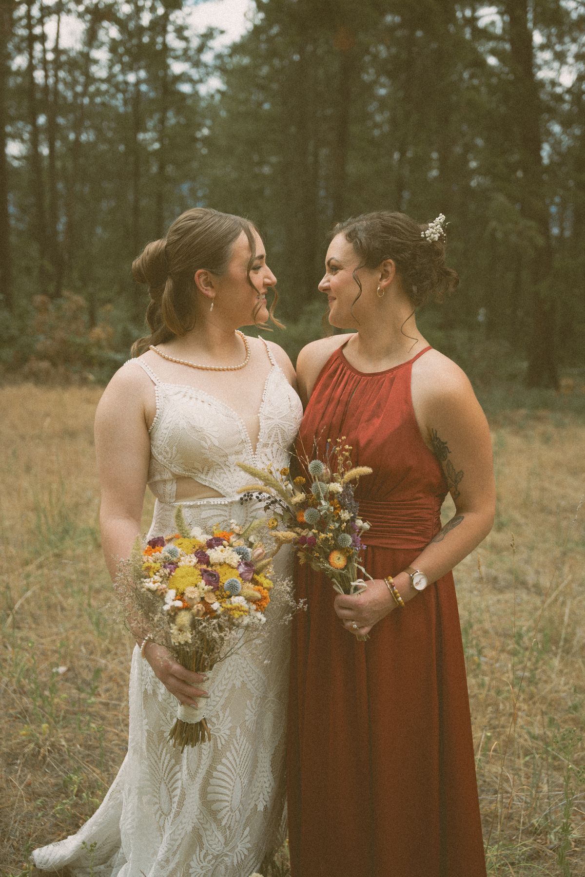 Bride with a bridesmaid in red holding wildflower bouquets in the forest