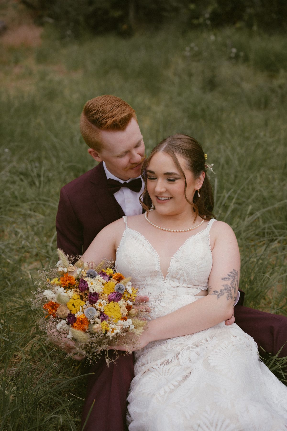 Gabby and Nicolas seated together on the grass with her bouquet